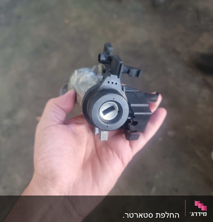 חלק חשמלי לרכב מוחזק ביד על רקע רצפה